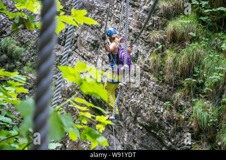 Femme pour traverser un pont de corde via ferrata dans les gorges de Postalm, Autriche. Le concept de parc aventure. Banque D'Images
