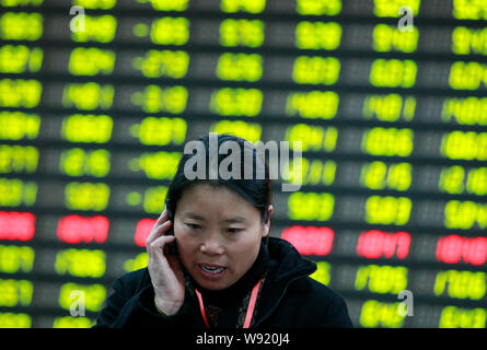 Un investisseur chinois parle sur son téléphone mobile devant un écran pour l'affichage des prix des actions (rouge pour l'augmentation des prix et la baisse des prix vert) à un Banque D'Images