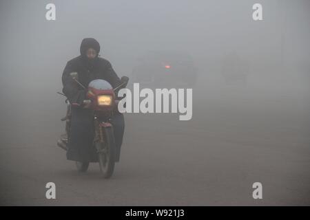 --FILE--un cycliste portant un masque en gros le smog dans Weihai, Chine de l'est la province de Shandong, 31 mars 2013. Le gouvernement central a mis son premier p Banque D'Images