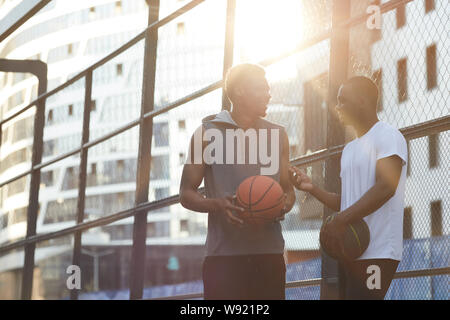 Portrait de deux hommes contemporains africains à discuter tout en se tenant dans la cour de basket-ball en plein air, copy space