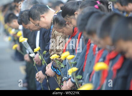 Les gens détiennent les fleurs comme ils observent une minute de silence pour commémorer les victimes de la 7.9-magnitude du séisme au Sichuan le 12 mai lors d'un deuil public e Banque D'Images