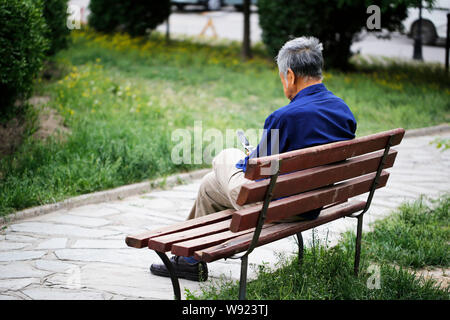 --FILE--un vieil homme chinois utilise son téléphone portable comme il est assis sur un banc seul à Beijing, Chine, 12 mai 2013. Une semaine après le continent chinois i Banque D'Images