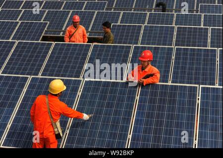 --FILE--travailleurs chinois vérifier les tableaux de panneaux solaires sur le toit d'un immeuble d'entreprises dans l'Est, Ningguo Chines Anhui province, 23 avril 2013. Banque D'Images