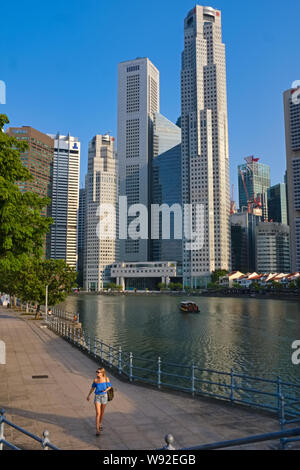 Une femme marche touristique le long Boat Quay, par la rivière Singapour, Singapour, les tours d'habitation du quartier d'affaires se dessinent dans l'arrière-plan Banque D'Images