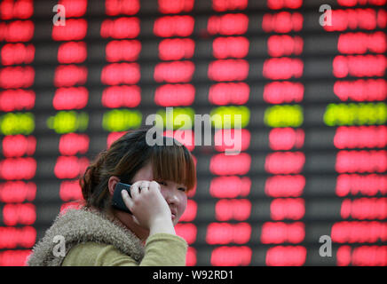 Un investisseur chinois parle sur son téléphone portable qu'elle en a l'air à des prix d'actions (rouge pour l'augmentation des prix et la baisse des prix vert) à une bourse Banque D'Images