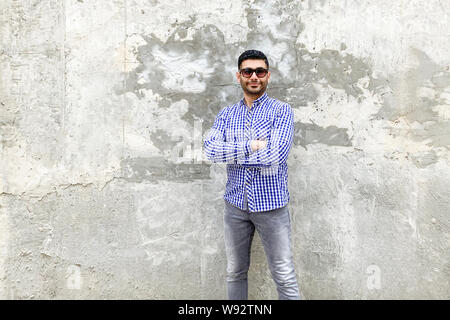 Portrait de beau jeune homme barbu avec succès avec des lunettes en chemise bleue à carreaux debout contre un mur gris béton. bras croisés et lookin Banque D'Images