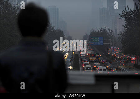 Un piéton se penche sur des masses de véhicules se déplaçant lentement dans un embouteillage dans le smog lourde à Beijing, Chine, 1 novembre 2013. Beijing est obligée de Banque D'Images