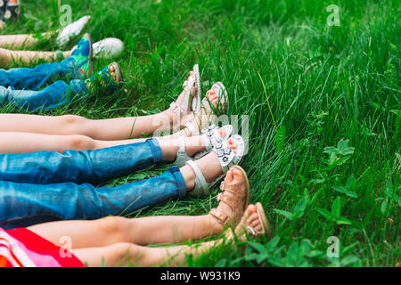 Les enfants allongés sur l'herbe verte dans le parc un jour d'été avec les jambes levées vers le ciel. Banque D'Images