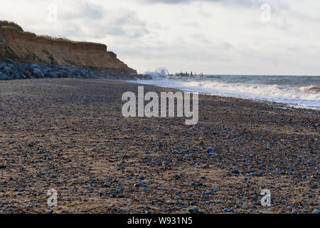 Les vagues de la mer du nord la mer se briser sur la protection de la défense fragils falaises de Happisburgh beach un soir d'été Banque D'Images