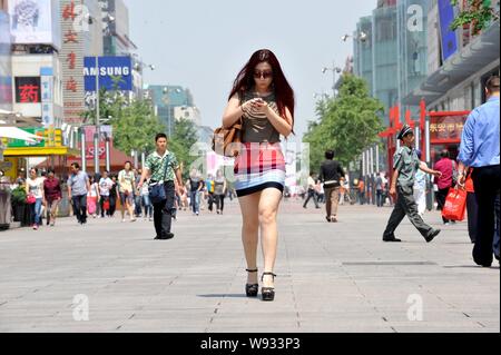 --FILE -- une jeune femme chinoise à la mode habillée d'une minijupe utilise son téléphone mobile comme elle marche le long de la rue commerçante de Wangfujing à Beijing, Chine, Banque D'Images