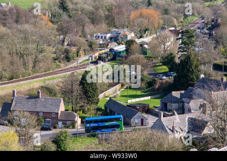 Château de Corfe, England, UK - 27 mars 2019 : Un Breezer bus double étage traverse le village de Corfe Castle Dorset tandis qu'un train à vapeur est Banque D'Images