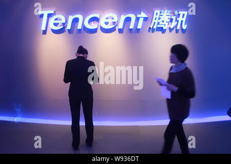 --FILE--un employé chinois, avant, une autre marche dernières en utilisant son téléphone portable en face d'une signalisation de Tencent à son siège dans la ville de Shenzhen, de sorte Banque D'Images