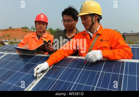 --FILE--travailleurs chinois vérifier les tableaux de panneaux solaires sur le toit d'un immeuble d'entreprises dans l'Est, Ningguo Chines Anhui province, 23 avril 2013. Banque D'Images