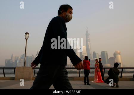 Un piéton portant un masque de visage passe devant un jeune couple qui pose pour des photos de mariage à la promenade sur le Bund dans le smog lourde à Shanghai, Chine, 2 Banque D'Images