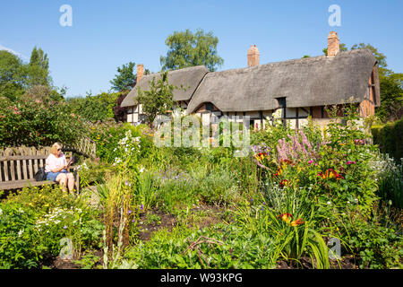 Anne Hathaway Cottage un cottage de chaume dans un jardin de chalet avec femme assis sur un banc Shottery près de Stratford upon Avon Warwickshire Angleterre GB Banque D'Images