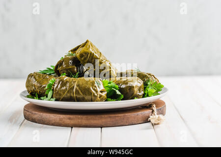 De délicieuses feuilles de vigne farcies (doom traditionnel cuisine Méditerranéenne Dolma) sur une plaque noire avec de la coriandre fraîche et l'aneth sur un parquet en bois clair backgrou Banque D'Images