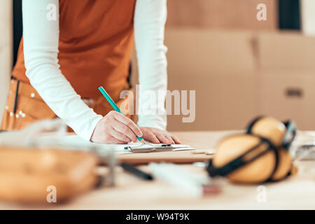 Female carpenter wearing bandana est écrit sur les notes du projet note de presse-papiers papier dans sa petite entreprise atelier de menuiserie Banque D'Images