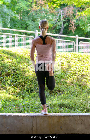 Athletic woman stretching exercices d'échauffement des muscles la jambe avant un entraînement équilibré sur un mur donnant sur verdure Banque D'Images