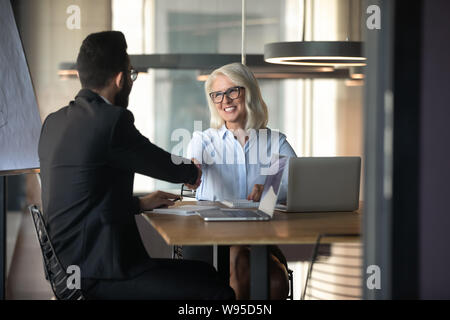Smiling mature woman shaking hand of young businessman Banque D'Images