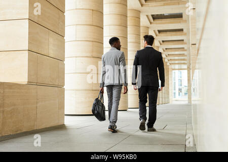 Vue arrière de deux jeunes collègues d'affaires en costumes d'aller travailler le long du corridor à l'extérieur Banque D'Images