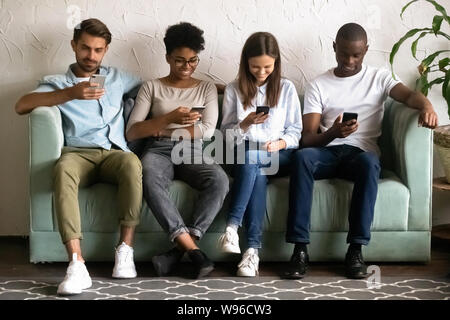 Les jeunes multiethniques asseoir dans la rangée à l'aide de téléphones cellulaires Banque D'Images