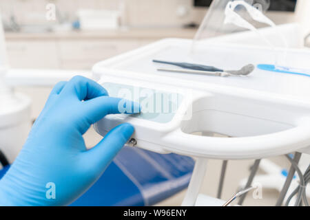 La main du dentiste dans la boîte à gants appuie sur les boutons de contrôle du président.. Travaux dentaires en clinique. Opération, remplacement des dents. Médecine, santé Banque D'Images