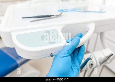 La main du dentiste dans la boîte à gants appuie sur les boutons de contrôle du président.. Travaux dentaires en clinique. Opération, remplacement des dents. Médecine, santé Banque D'Images
