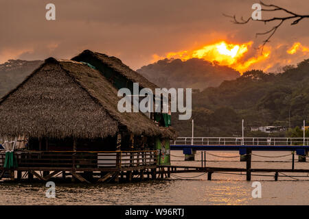 Coucher du soleil sur un toit de chaume restaurant le long de la rive du lac Catemaco au coucher du soleil à Catemaco, Veracruz, Mexique. Le lac d'eau douce tropical au centre de la Sierra de Los Tuxtlas, est une destination touristique populaire et connu pour libre allant des singes, la forêt tropicale et de sorcières mexicain connu sous le nom de Brujos. Banque D'Images