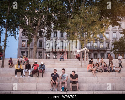 LYON, FRANCE - 18 juillet 2019 : les Français, surtout les hommes assis sur la rive du Rhône (quais) dans la soirée, boire de l'alcool tandis que les gens sont Banque D'Images