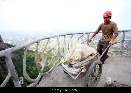 Un travailleur transporte des matériaux de construction sur une route en construction sur la falaise de Shifo Shiniuzhai Mountain dans le comté de Pingjiang dans endroit pittoresque, Banque D'Images