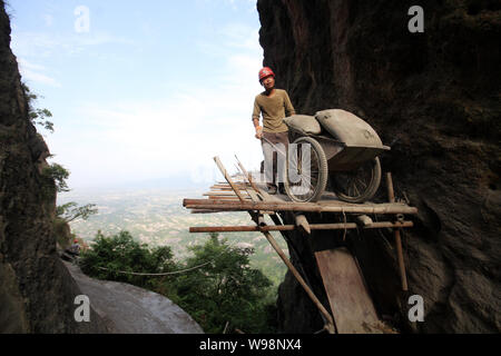 Un travailleur transporte des matériaux de construction sur un chemin en bois pour construire une route sur la falaise de Shifo en montagne l'endroit pittoresque Shiniuzhai en pays Pingjiang Banque D'Images