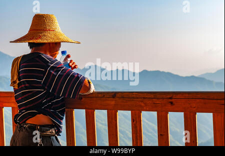 Un homme de la minorité autochtone Zhuang regardant le paysage de montagne dans la région de Ping An après une dure journée de travail, Longsheng county, Guangxi, Chine. Banque D'Images