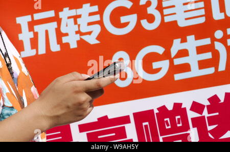 --FILE--une jeune femme chinoise utilise son téléphone mobile devant une affiche pour les services 3G à Haikou City, province de Hainan, Chine du Sud 13 septembre 20 Banque D'Images