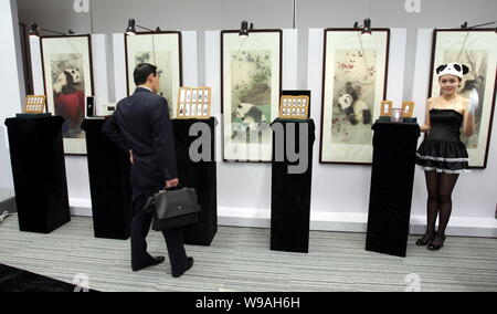 Un visiteur regarde panda d'or et d'argent sur le thème des bars pour l'Exposition Universelle de 2010 en face de peintures de l'Expo 10 pandas lors d'une cérémonie de lancement à l'al. Banque D'Images