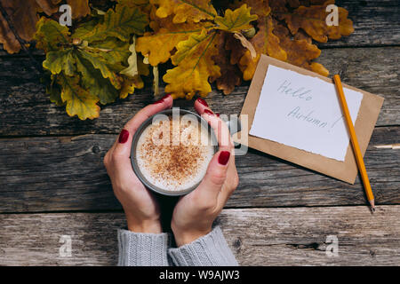 Début d'automne encore la composition de la vie. Woman's hands avec une tasse de café, cappuccino, ce dernier. Les feuilles d'automne, de l'artisanat et de l'enveloppe papier avec texte Bonjour Banque D'Images