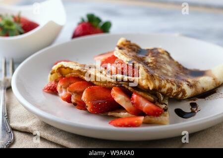 Crêpes avec les tranches de fraises et chocolat topping imparfaitement servi sur plaque blanche Banque D'Images