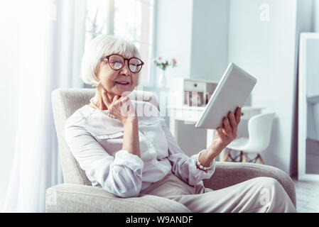 Transmission à la retraite élégante woman holding tablet tout en regardant des photos de famille Banque D'Images