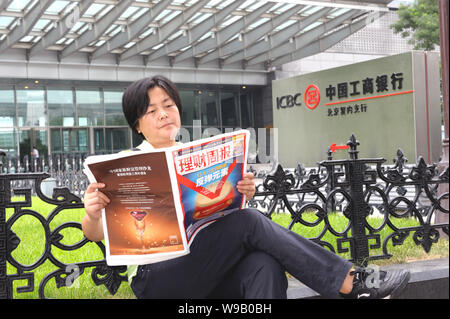 Une femme chinoise journal se lit à l'extérieur une succursale de la Banque industrielle et commerciale de Chine (ICBC), à Beijing, Chine, le 2 août 2010. Industrial & Com Banque D'Images