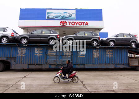 --FILE--un Chinois chevauche son vélo électrique cours des voitures de Toyota d'être transportés à l'extérieur d'un concessionnaire Toyota à Xiangfan City, Hubei Chines centrale pr Banque D'Images