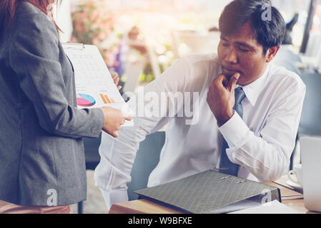 Asian Businessman thinking du compte de profits et pertes sur nouveau projet. Jeune secrétaire montrant rapport financier. Banque D'Images