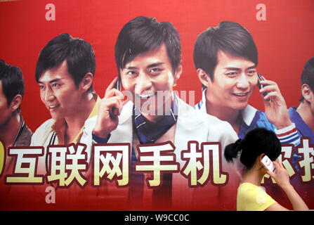 --FILE--une jeune femme chinoise à parler sur son téléphone portable passe devant une publicité pour les téléphones mobiles dans la ville de Shiyan, province de Hubei, Chine centrale Banque D'Images