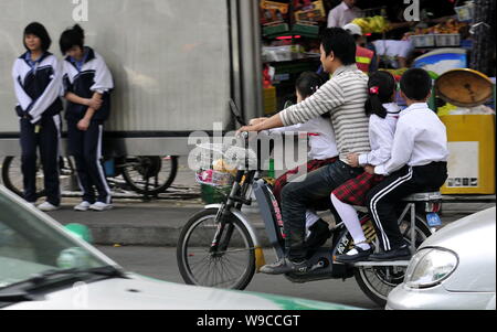 --FILE--un Chinois chevauche son vélo électrique portant trois élèves dans une rue de la ville de Shenzhen, province de Guangdong, en Chine du sud 16 Février 2009 Banque D'Images