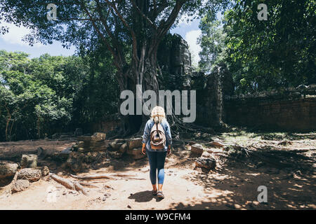 Young blonde woman découvrir les ruines du temple d'Angkor Wat à Siem Reap, Cambodge. Arbre qui pousse sur le toit de l'arc porte d'entrée du temple Banque D'Images