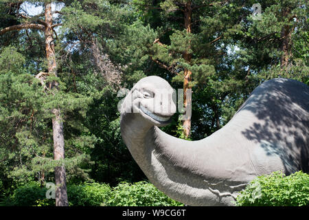 Dessin animé dinosaure bon gris avec un long cou est sorti de la forêt de conifères sur une journée d'été et les sourires, la sculpture de brachiosaure Banque D'Images