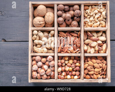 Boîte en bois avec différents types d'écrous sur un fond de bois sombre. Vue d'en haut Banque D'Images