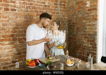 Vlogger et blogueur freelance, food concept. Young caucasian couple cooking together et l'enregistrement de la vidéo en direct de vlog et médias sociaux avec appareil photo professionnel contre mur de brique dans la cuisine. Banque D'Images