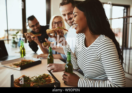 Laughing young African American Woman avec les collègues dans un bureau après le travail de manger des pizzas et boire une bière Banque D'Images