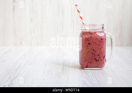 Mason bocal verre mug rempli de banane, cassis, smoothie au lait de coco sur un fond en bois blanc, vue de côté. L'espace pour le texte. Banque D'Images