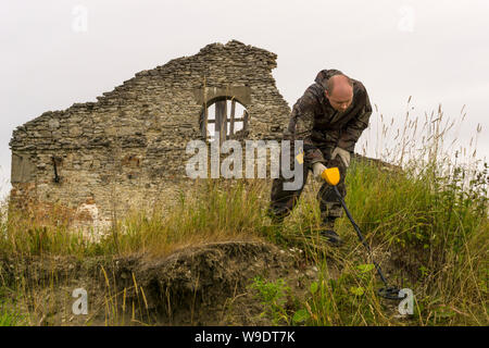 Homme avec un détecteur de métal balaie la terre sur un fond de ruines antiques Banque D'Images