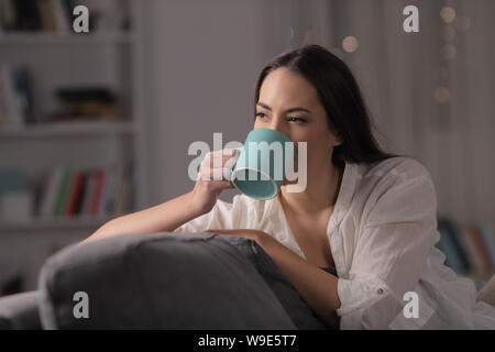 Dame de boire du café assis sur un canapé dans la nuit à la maison Banque D'Images